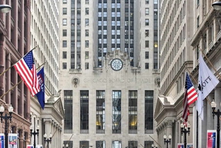 Facade of the Chicago Board of Trade Building on LaSalle Street, with its clock, carved figures, and the Chicago Board of Trade inscription above the entrance, flanked by American flags
