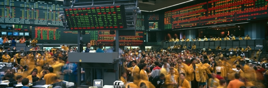 Futures trading floor with traders in yellow jackets and electronic price boards displaying derivatives markets