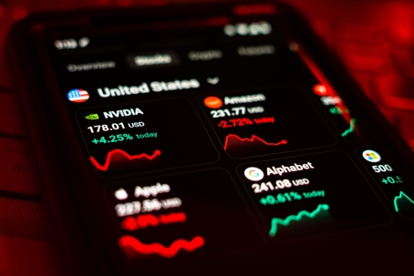 Smartphone displaying a mobile trading app with U.S. stock prices and trend lines, lit in red.