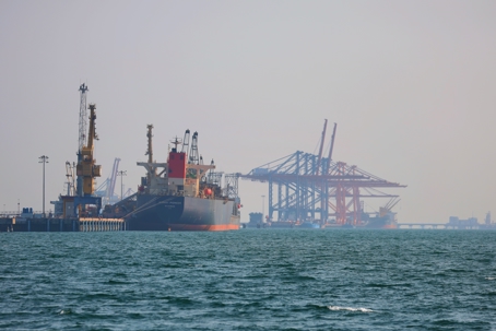 Cargo vessel at port in haze, with cranes and industrial infrastructure partially obscured by fog