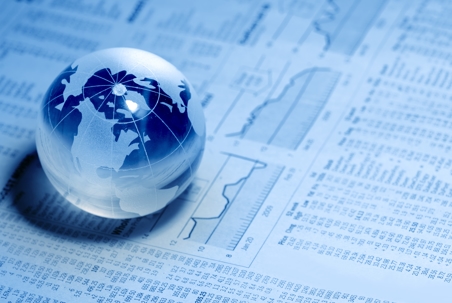 Glass globe resting on financial data and stock charts, symbolizing global markets and continuous trading activity.