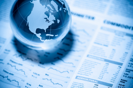 Crystal glass globe resting on a newspaper commodities page showing agricultural futures prices, representing global markets and derivatives regulation