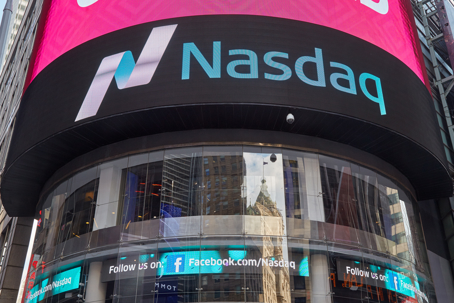 Exterior view of the Nasdaq MarketSite at One Times Square in New York City, featuring the curved black facade with the teal Nasdaq logo and wordmark displayed prominently on the large LED screen, with lower ticker displays visible along the base of the bu